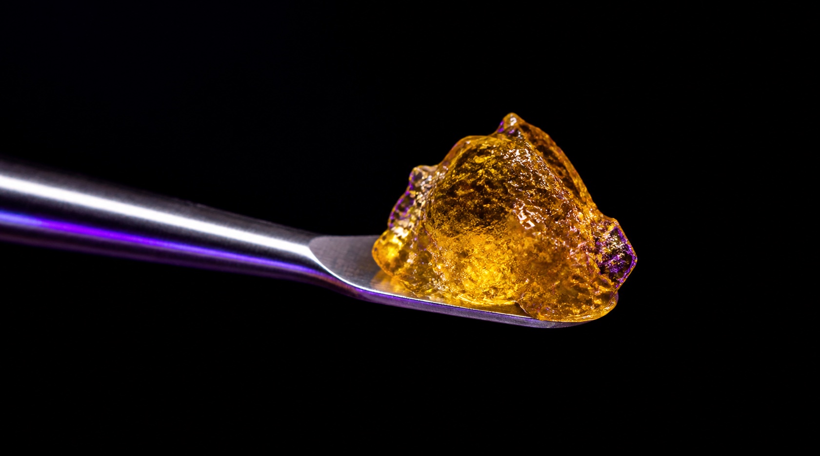 Golden cannabis concentrate on a metal tool against a dark background